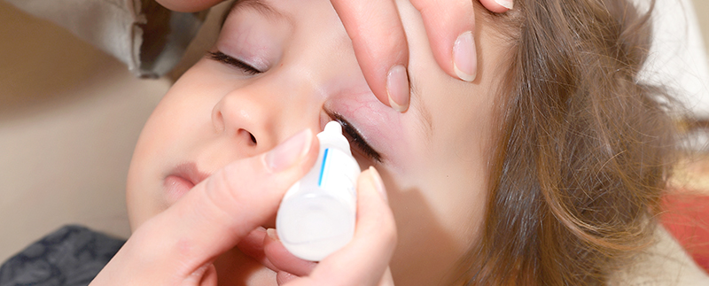 Person applying eye drops to a young child using a dropper squeeze bottle with matching dropper tip fitments and caps