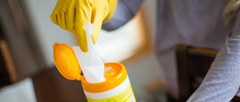 person using cleaning product canister for antibacterial wipes wearing yellow gloves